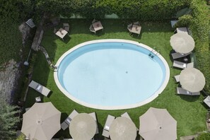 Una piscina ovalada rodeada por un césped bien cuidado, con varias sillas de descanso y sombrillas dispuestas alrededor del borde.