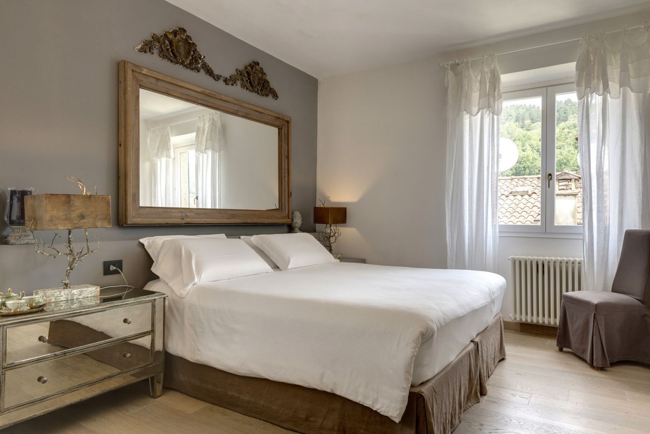 A bedroom with a large bed, bedside tables, a mirror, a radiator, and a window with curtains.