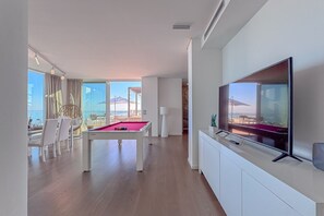 Uma sala de estar moderna com mesa de bilhar, televisão de tela plana e varanda com vista para o mar.