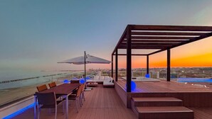 A wooden deck with a dining table and chairs, a sofa, and a pergola.