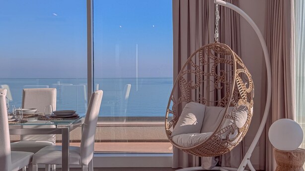 A balcony with a dining table set, a hanging chair, and a view of the sea.