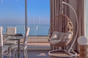 Un balcón con mesa y sillas, una silla colgante y vista al mar.