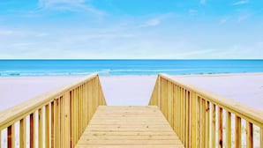 Un paseo marítimo de madera que lleva a una playa bajo un cielo despejado.
