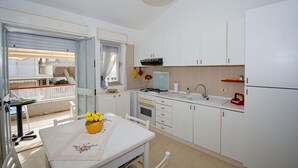 Cocina compacta con alacenas blancas, estufa a gas, lavamanos y comedor con mesa y sillas.