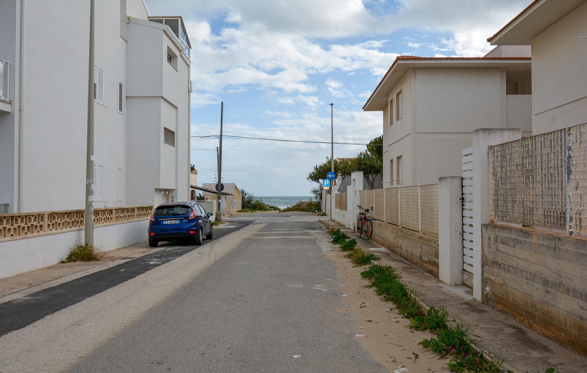 Une rue étroite bordée de bâtiments blancs, avec une voiture garée et un vélo.