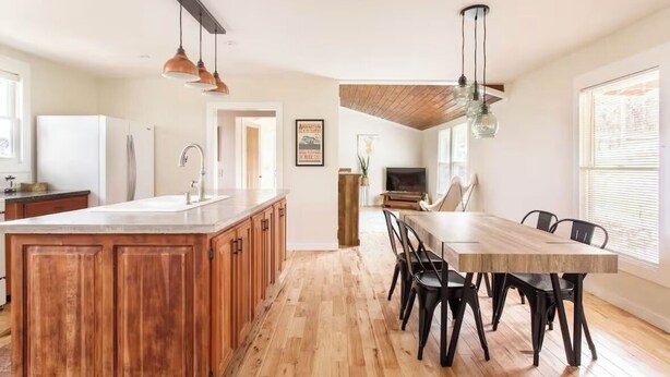 Una cocina amplia con armarios de madera, una isla central y una zona de comedor con una mesa larga y sillas.