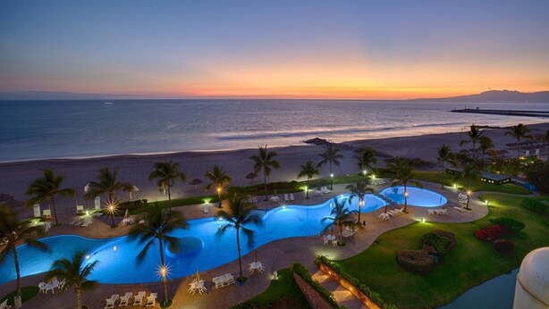 A resort with a large pool area, palm trees, and a view of the ocean at sunset. - Mayan Island Horizonte 303 Calakmul (Nuevo Nayarit)