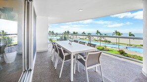 Un balcon avec une table et des chaises, donnant sur une piscine et une plage.