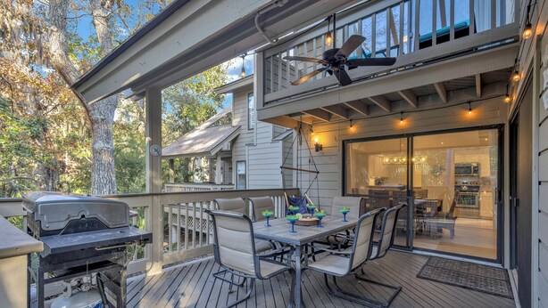 Eine überdachte Terrasse mit Grill, Sitzgelegenheiten und Deckenventilator.