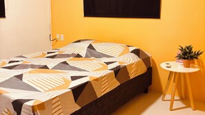A bedroom with a bed, a small table with a plant, and a window with a black blind. - Vacation apartment with pool  (Willemstad)