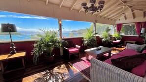 Una habitación acogedora con techo de madera, un candelabro, vista al mar y varias plantas en macetas.