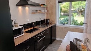 A modern kitchen with a microwave, oven, sink, and black cabinetry. There is a window with a view of greenery outside. - Nine on Cochrane - relax, unwind and explore Rotorua. (Rotorua)