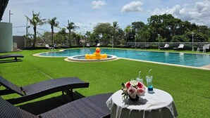 A pool area with artificial grass, lounge chairs, and a table with drinks and flowers. - First Pacific Cirrus - Pattaya (Pattaya)