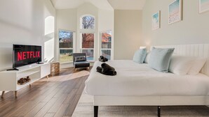 A modern bedroom with a large bed, a TV on a stand, and a view of the outdoors through large windows. - Private Pool Resort, Cinema, Hot Tub & Game Room (North Richland Hills)