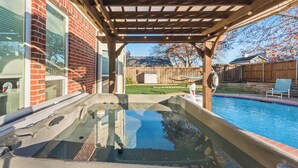 A backyard with a hot tub, a wooden pergola, a swimming pool, and a brick house. - Private Pool Resort, Cinema, Hot Tub & Game Room (North Richland Hills)