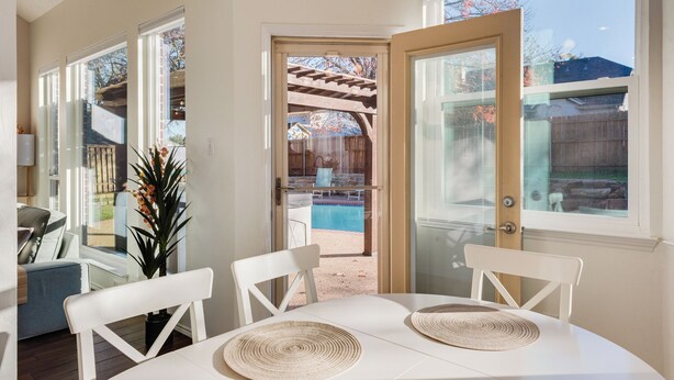 A dining area with a table and chairs, a potted plant, and a view of a backyard with a pool. - Private Pool Resort, Cinema, Hot Tub & Game Room (North Richland Hills)