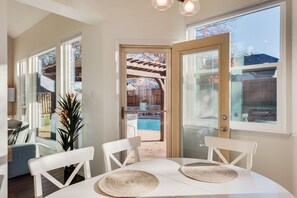Ein Essbereich mit Tisch und Stühlen, einem Blumentopf und Blick auf einen Hinterhof mit Pool.