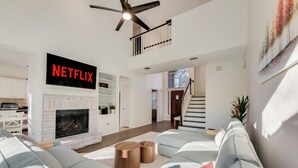 A modern living room with a fireplace, a Netflix sign, a staircase, and a large sofa. - Private Pool Resort, Cinema, Hot Tub & Game Room (North Richland Hills)