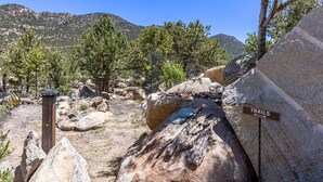 Un sendero rocoso con un cartel que indica rutas, rodeado de grandes rocas y árboles.
