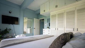 A bedroom with a bed, a TV mounted on the wall, a dresser, and a wardrobe.