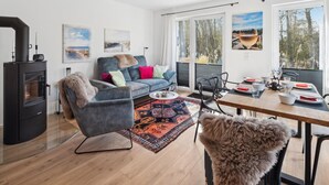 A modern living room with a sofa, a dining table set for two, a fireplace, and large windows with a view of trees. - 2 bedroom awesome home in Tossens (Tossens)