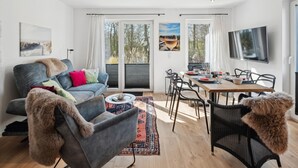 A modern living room with a grey sofa, a dining table set for four, and a large TV on the wall. - 2 bedroom awesome home in Tossens (Tossens)