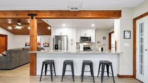 A modern kitchen with white cabinets, a stainless steel refrigerator, a microwave, and a granite countertop. There are four black stools at the counter. - MTNSIDE Cabin with VIEWS by LYNX LAKE 20 min to TOWN (Prescott)