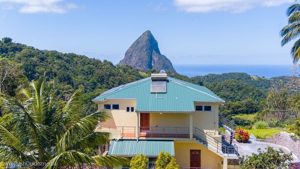Un bâtiment à deux étages surmonté d’un toit végétalisé, entouré d’une végétation luxuriante et avec une montagne imposante en arrière-plan.