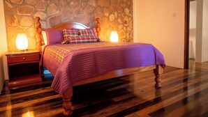 Une chambre avec un mur en pierre, un cadre de lit en bois et une table de chevet avec une lampe.