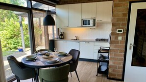Una cocina compacta con armarios blancos, microondas y cocina a gas. Hay una mesa de comedor con sillas y una lámpara colgante.