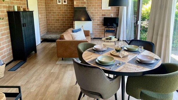 Una sala de estar moderna con pared de ladrillo, chimenea, un sofá y un comedor con una mesa preparada para dos.