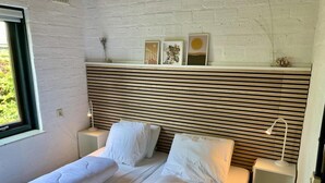 Una cama doble con ropa de cama blanca, cabecero con listones, mesitas de noche con lámparas y una obra de arte en la pared.