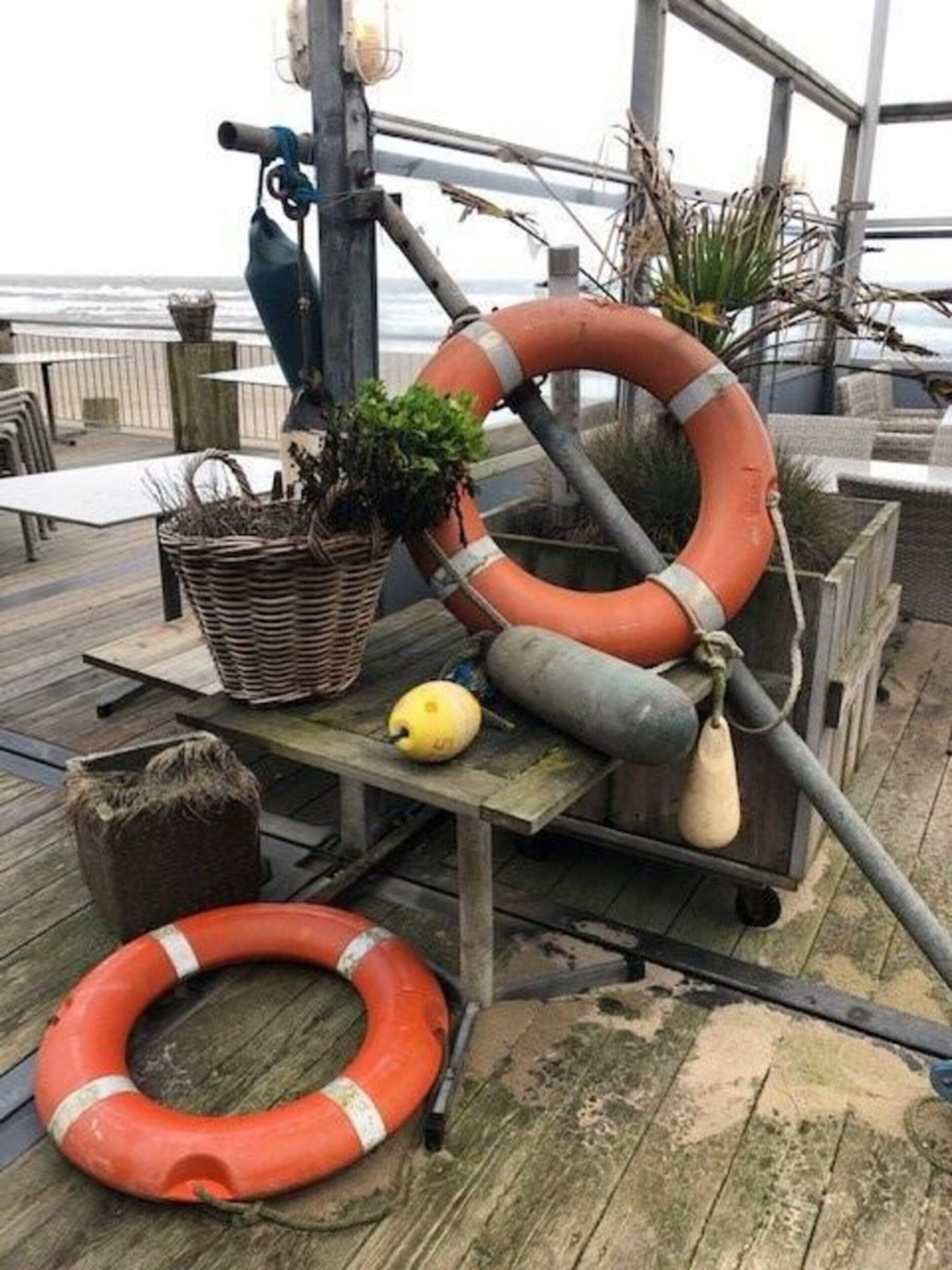 Eine Holzterrasse mit einem Rettungsring, einem gelben Ball und einem Korb mit Pflanzen.