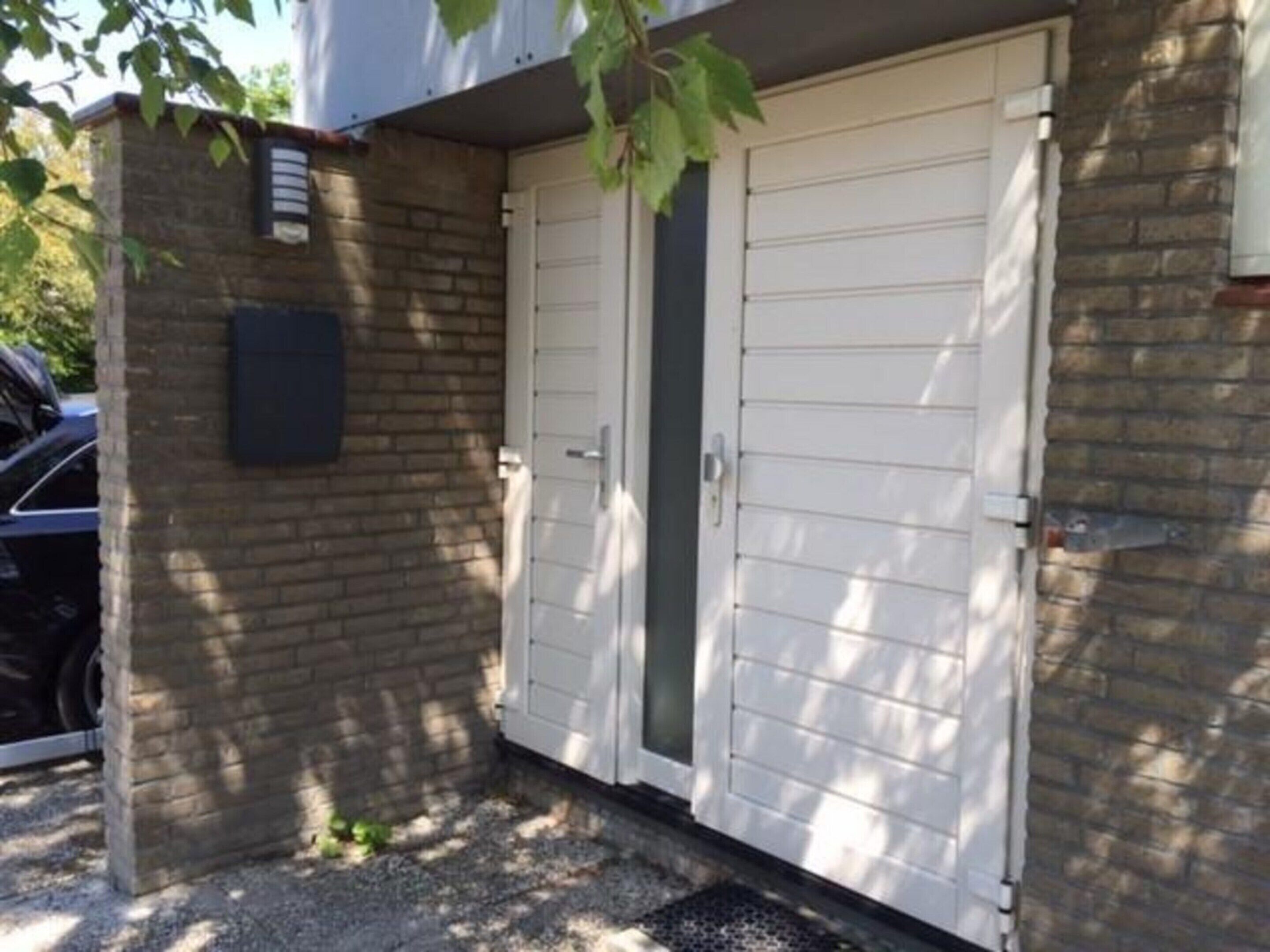 Een dubbele garagepoort met een kleine bakstenen muur en een metalen ventilatie rooster.