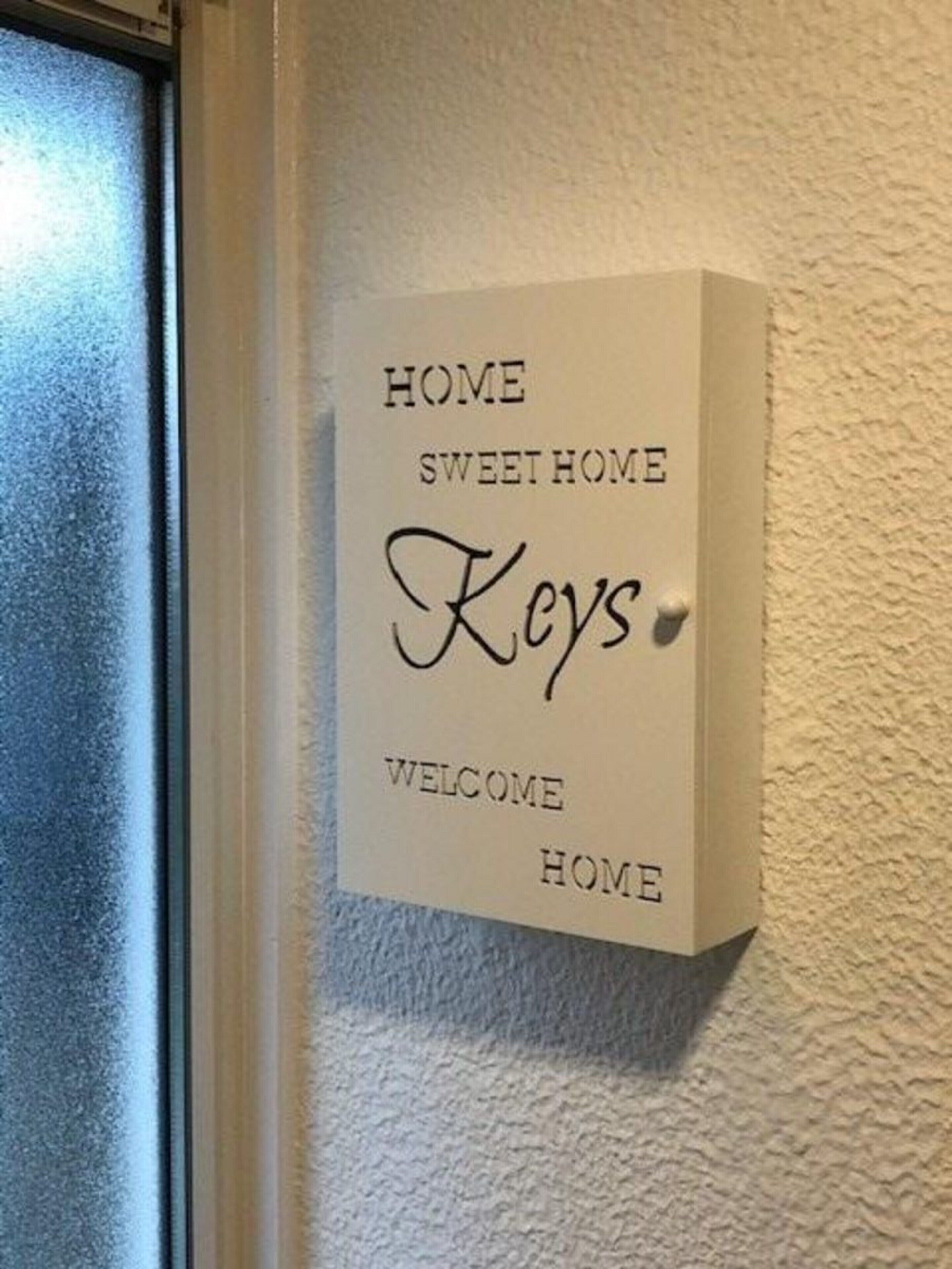 A welcome sign with the text "HOME SWEET HOME Keys Welcome HOME" mounted on a textured wall.