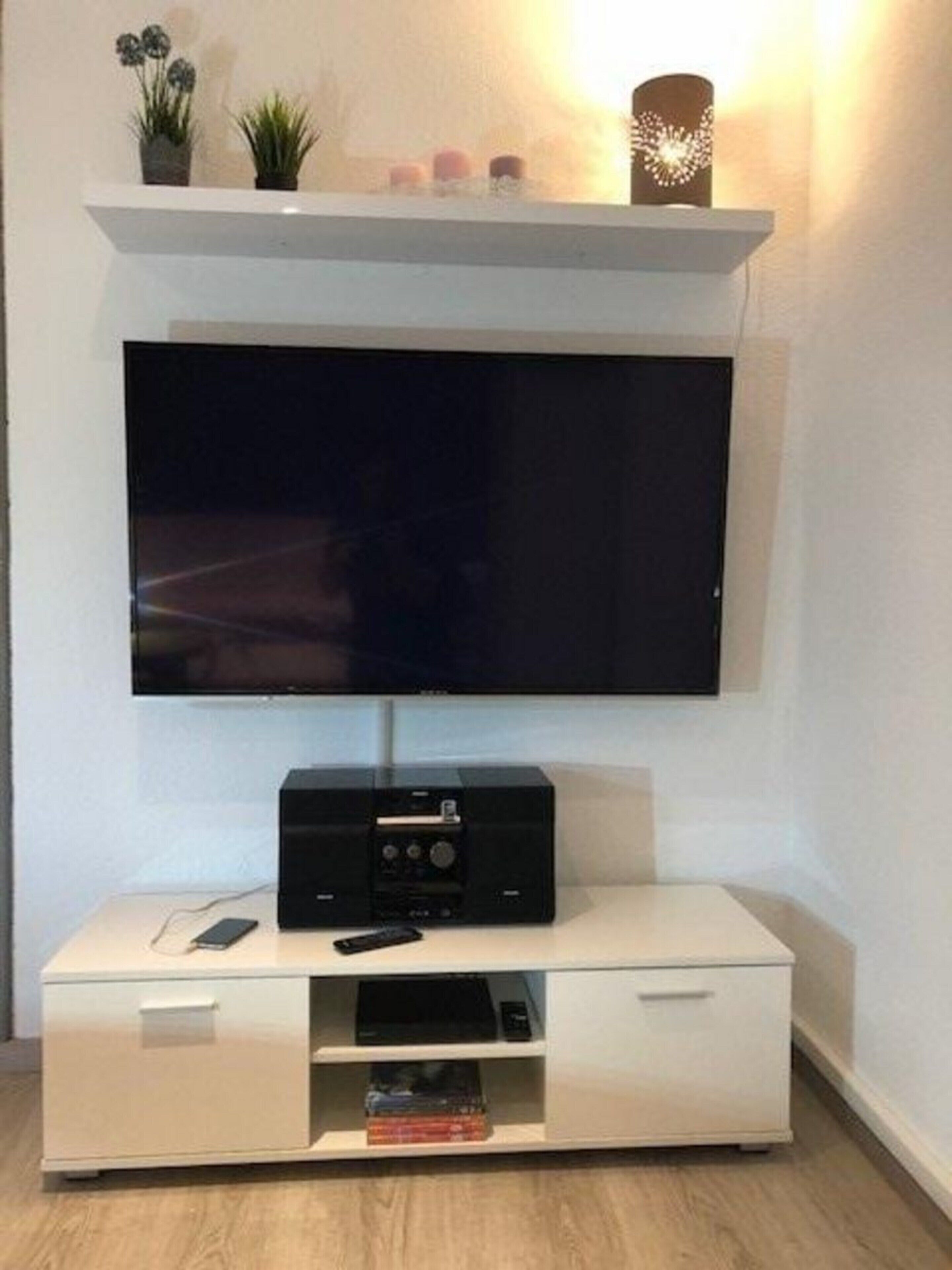 Un televisor de pantalla plana montado en una pared blanca, con un mueble de entretenimiento negro debajo.