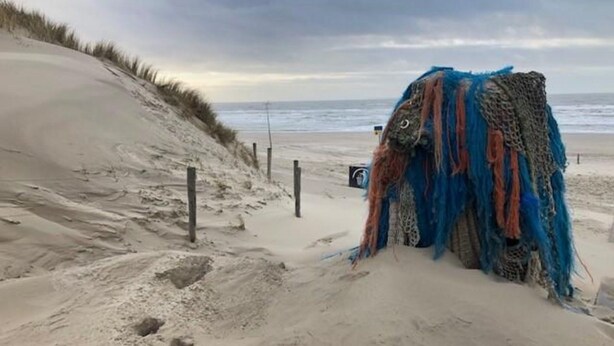 Ein sandiger Strand mit einer großen, farbenfrohen, abstrakten Skulptur im Vordergrund.