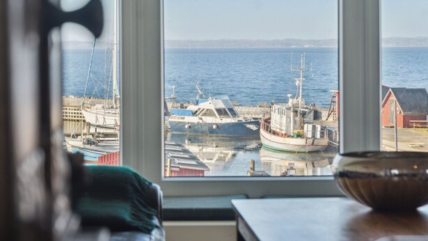 Blick durch ein Fenster auf einen Hafen mit vertäuten Booten, ein rotes Gebäude und ein klarer Himmel.