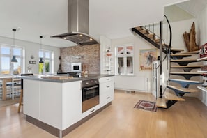 A modern kitchen with a central island, a brick wall, and a spiral staircase.