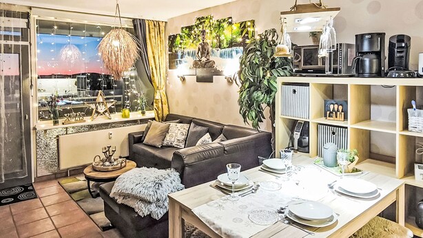 A modern living room with a sofa, dining table set for four, and a kitchen area with appliances and plants. - Bocksbergperle 3 by Interhome (Hahnenklee)