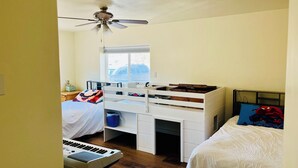 Una camera da letto con un letto a castello, una scrivania, una tastiera e una ventola a soffitto.