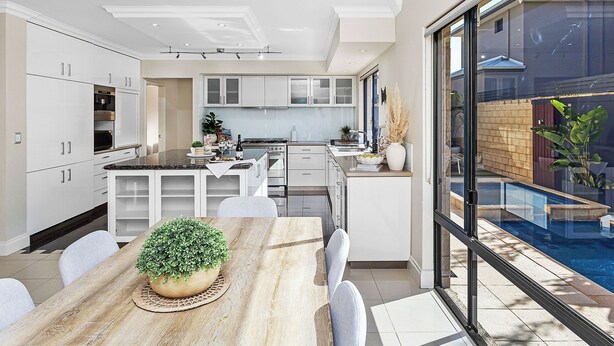 Een moderne keuken met witte kasten, een centraal eiland en een eethoek met een houten tafel en stoelen.