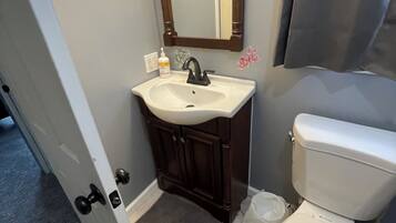 Een badkamer met een wit wastafel, een donker houten wastafelmeubel, een spiegel en een toilet.