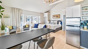 A modern kitchen with a stainless steel refrigerator, a dining area with a long table and chairs, and a living area with a sofa and a large window.