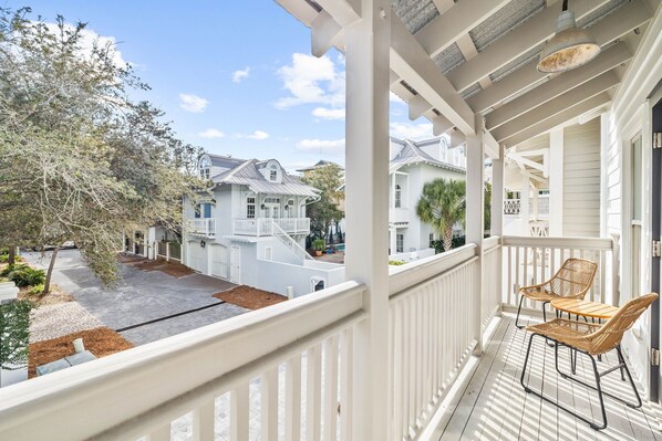 A covered porch with two wicker chairs, a view of a residential street, and a clear sky.