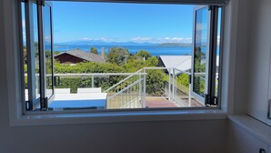 A room with a large window offering a view of a mountainous landscape and the sea. - HILLTOP, CENTRAL, QUIET, LOCATION WITH STUNNING LAKE AND MOUNTAIN VIEWS. (Taupō)