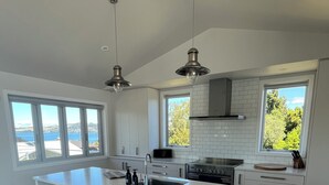A modern kitchen with a large island, white cabinetry, and a view of the sea. - HILLTOP, CENTRAL, QUIET, LOCATION WITH STUNNING LAKE AND MOUNTAIN VIEWS. (Taupō)