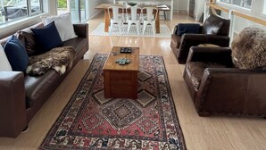 A spacious living room with a large sofa, a coffee table, and a rug. There is a dining area with a table and chairs in the background. - HILLTOP, CENTRAL, QUIET, LOCATION WITH STUNNING LAKE AND MOUNTAIN VIEWS. (Taupō)