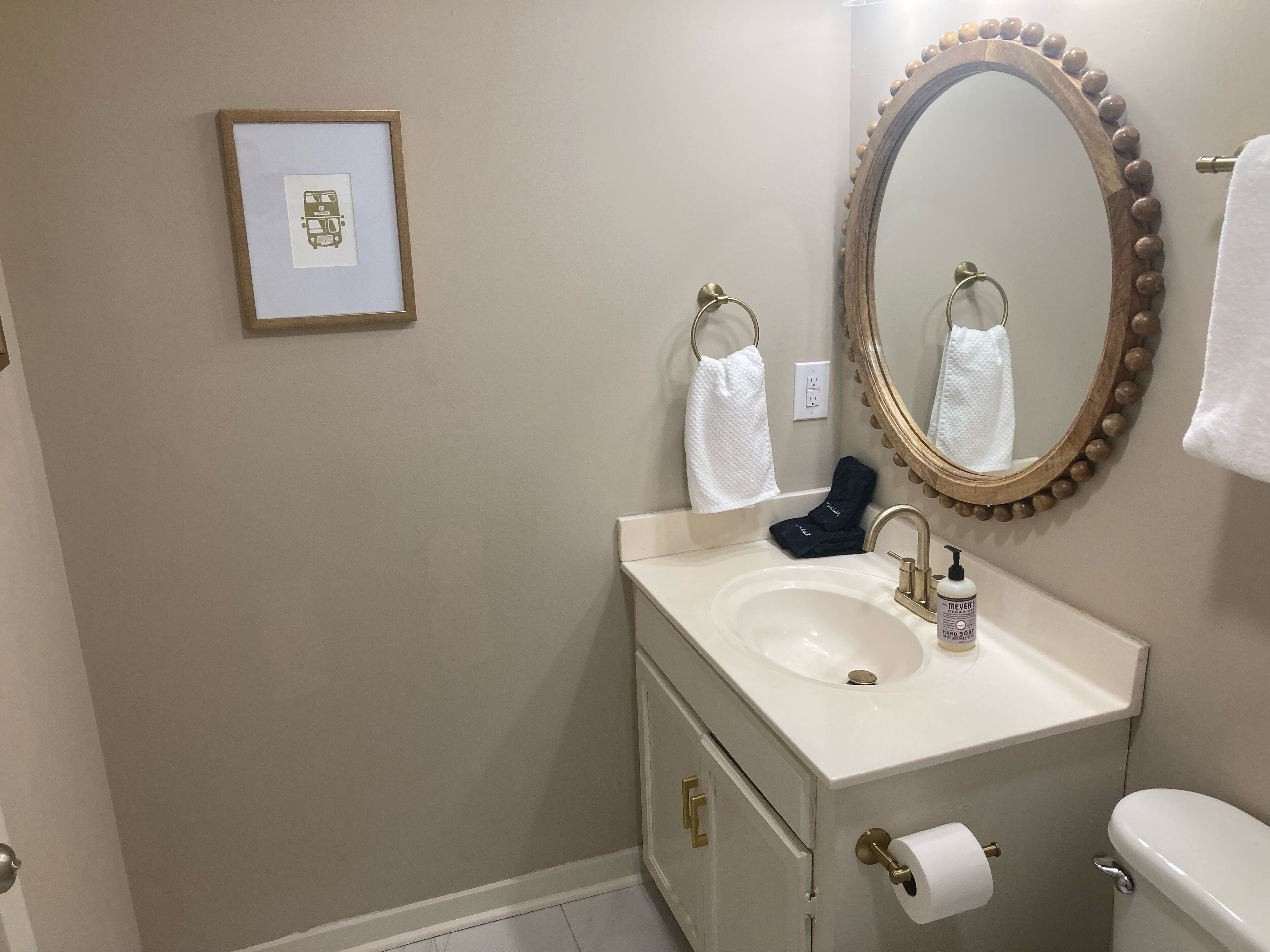 A bathroom with a sink, mirror, toilet, and framed picture on the wall.