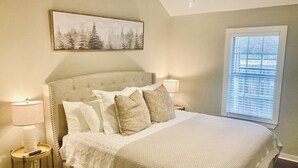 Una camera da letto con un letto grande, una testiera, lampade sui comodini, una finestra con persiane e un quadro appeso al muro.